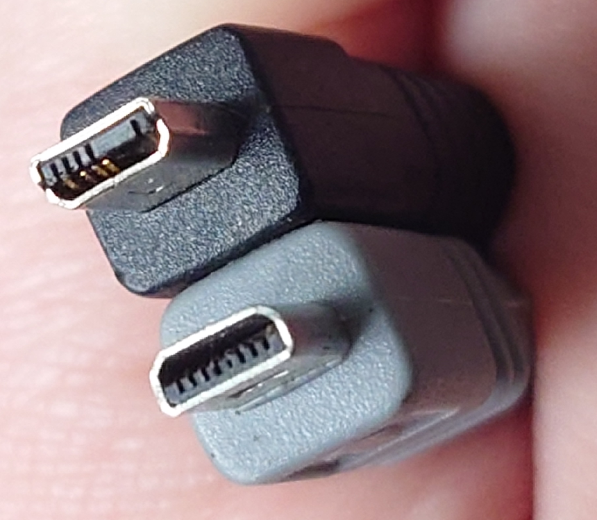 A hand holding two similar, but different, USB interface cables